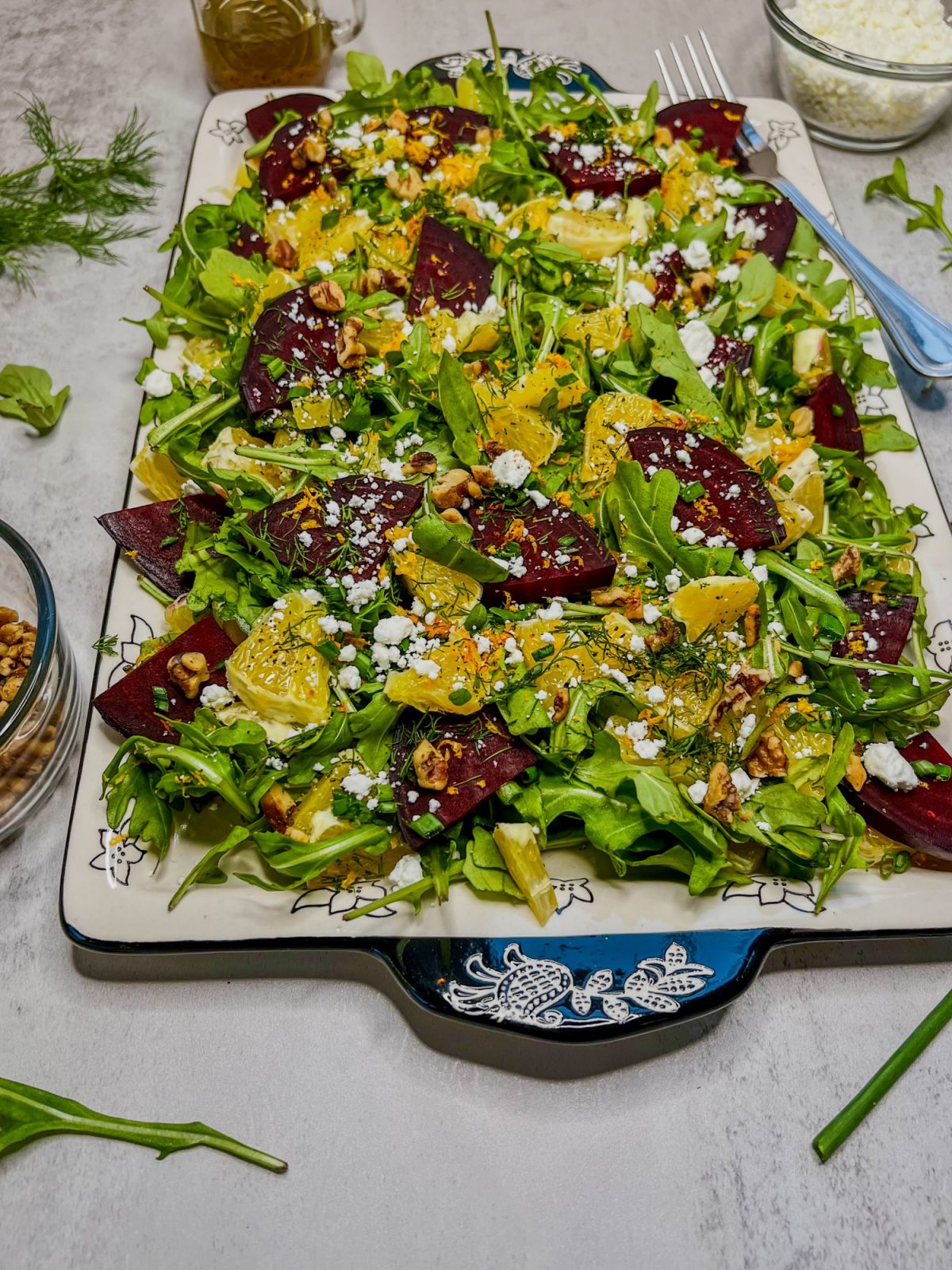 Arugula beet salad on a serving tray with some dressing and goat cheese off to the side