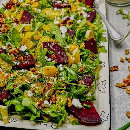 Arugula beet salad on a serving tray with some dressing and goat cheese off to the side