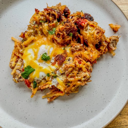 Pulled pork breakfast skillet on a white plate on a wooden table