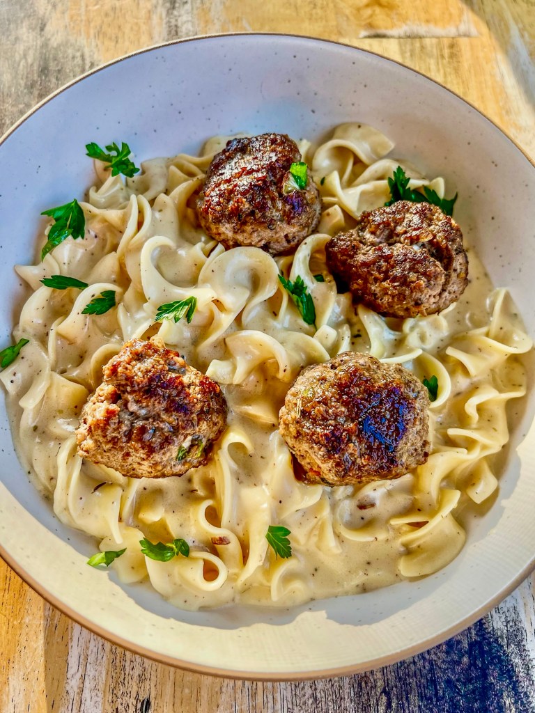 Swedish meatballs in a white bowl with some parsley for garnish, on a wooden table