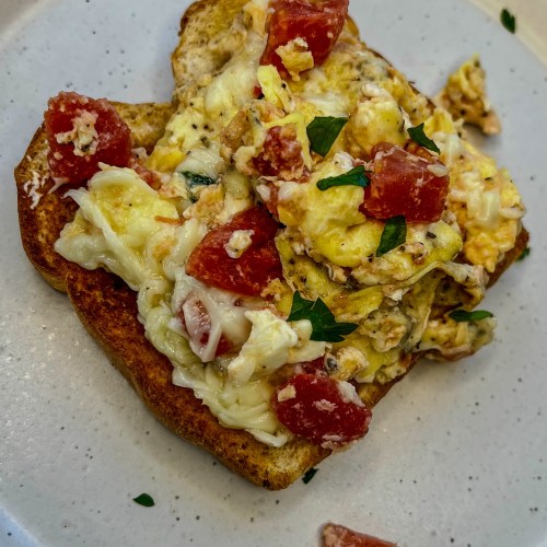 Tomato and feta scrambled eggs on a white plate on a wooden table