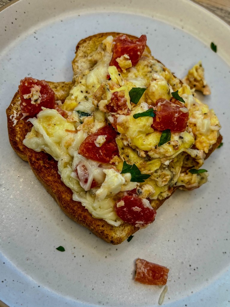Tomato and feta scrambled eggs on a white plate on a wooden table