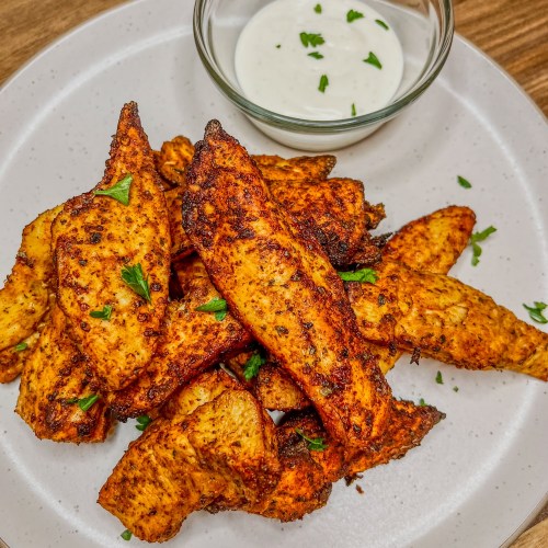 Air fryer chicken tenders on a white plate with a small dish of ranch next to it