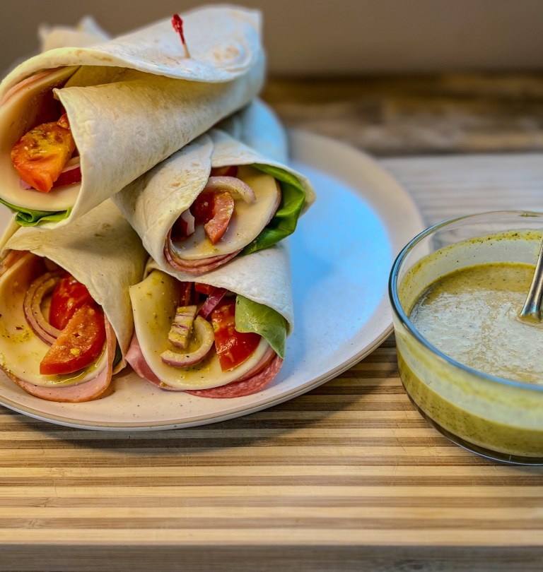 A plate of Italian Wraps on a wooden table with a dish of Italian Dressing nearby