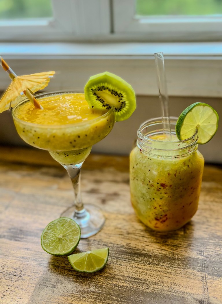 Kiwi Mango Daiquiri in a glass with a mason jar with more next to it with some kiwi and lime garnishes