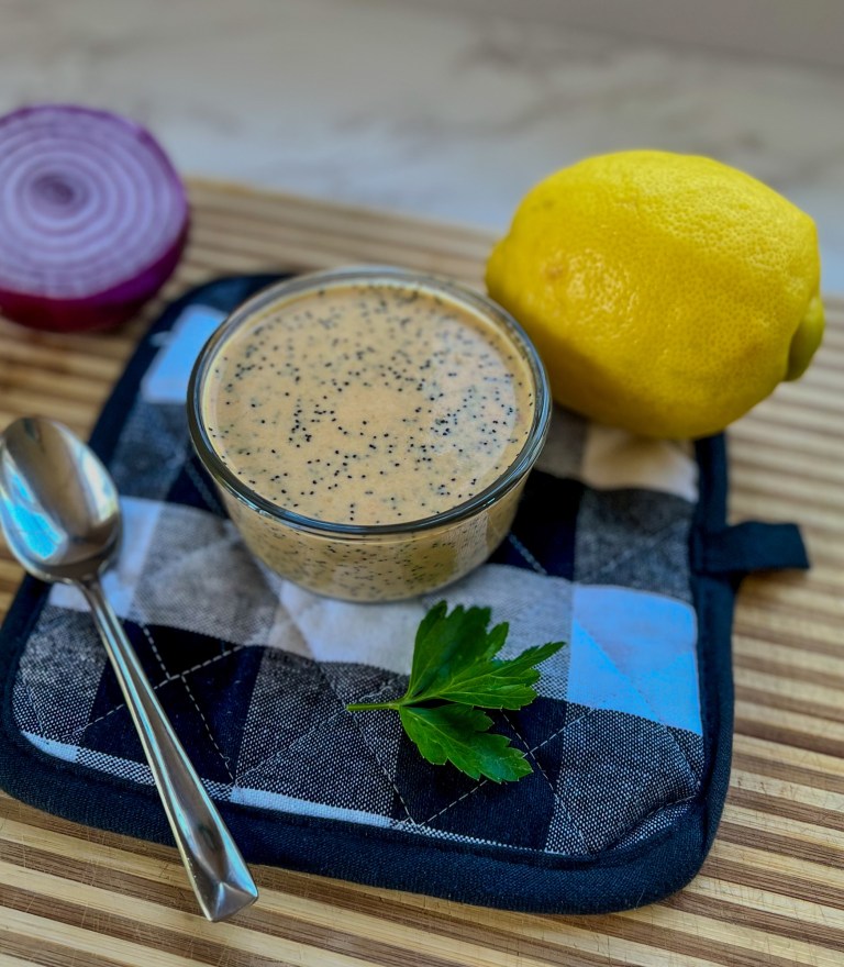 Lemon Poppy Seed Dressing in a ramekin on a hot pad with some lemon and onion next to it