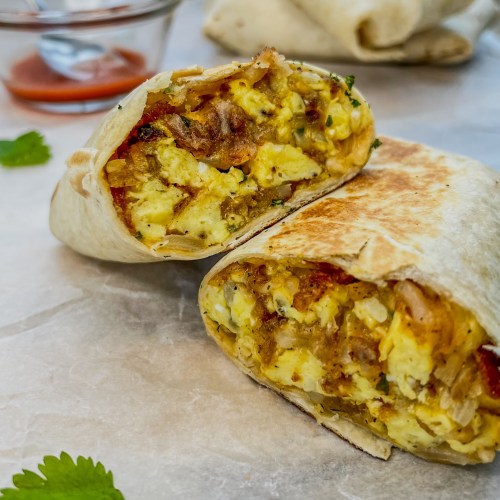 Meal prep breakfast burritos with some cilantro scattered around and hot sauce off to the side