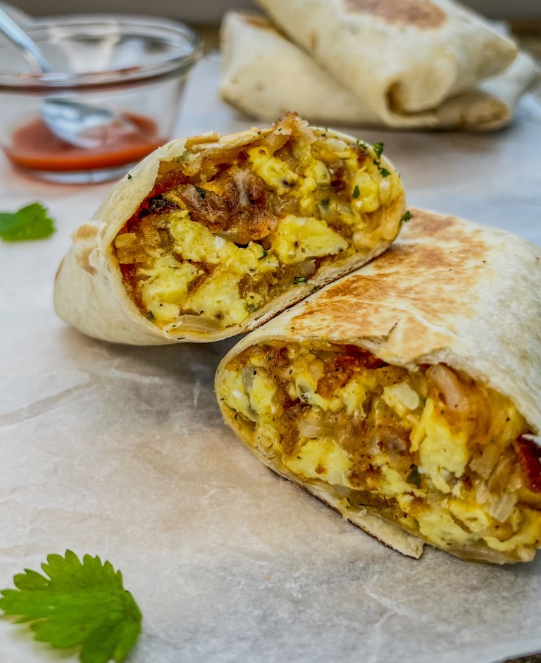 Meal prep breakfast burritos with some cilantro scattered around and hot sauce off to the side