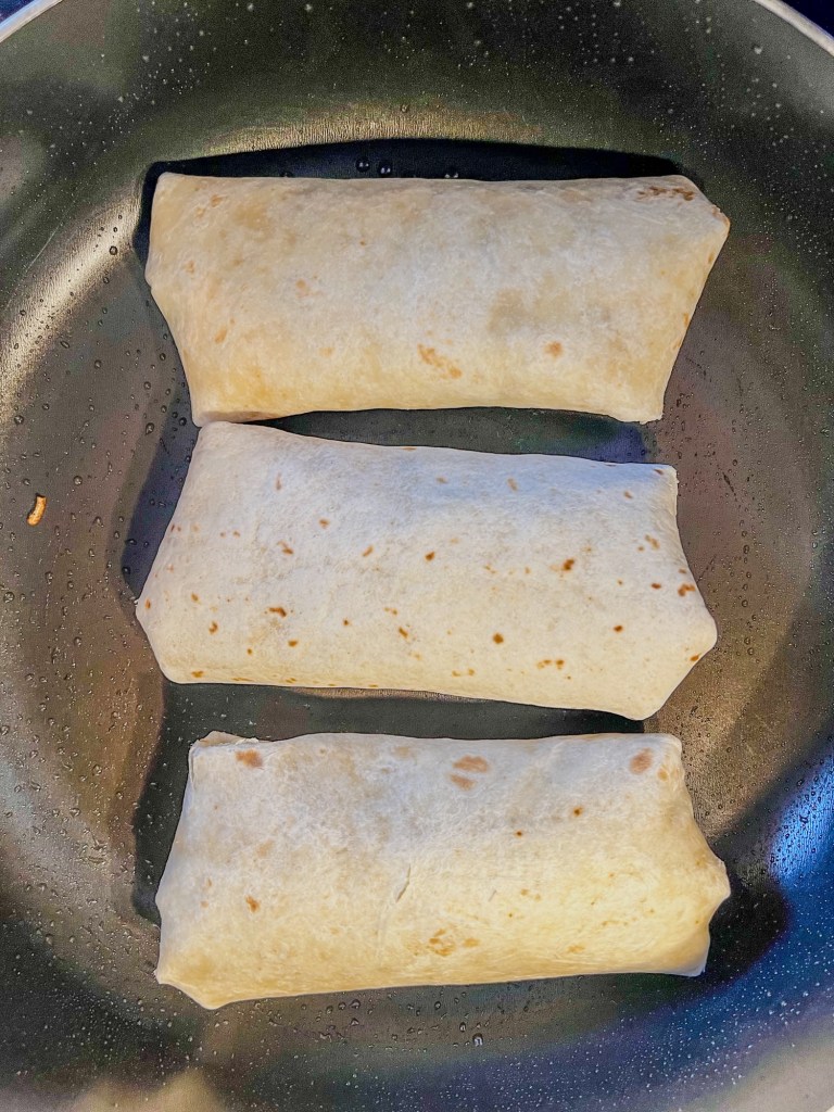 Breakfast burritos toasting in a skillet on the stove