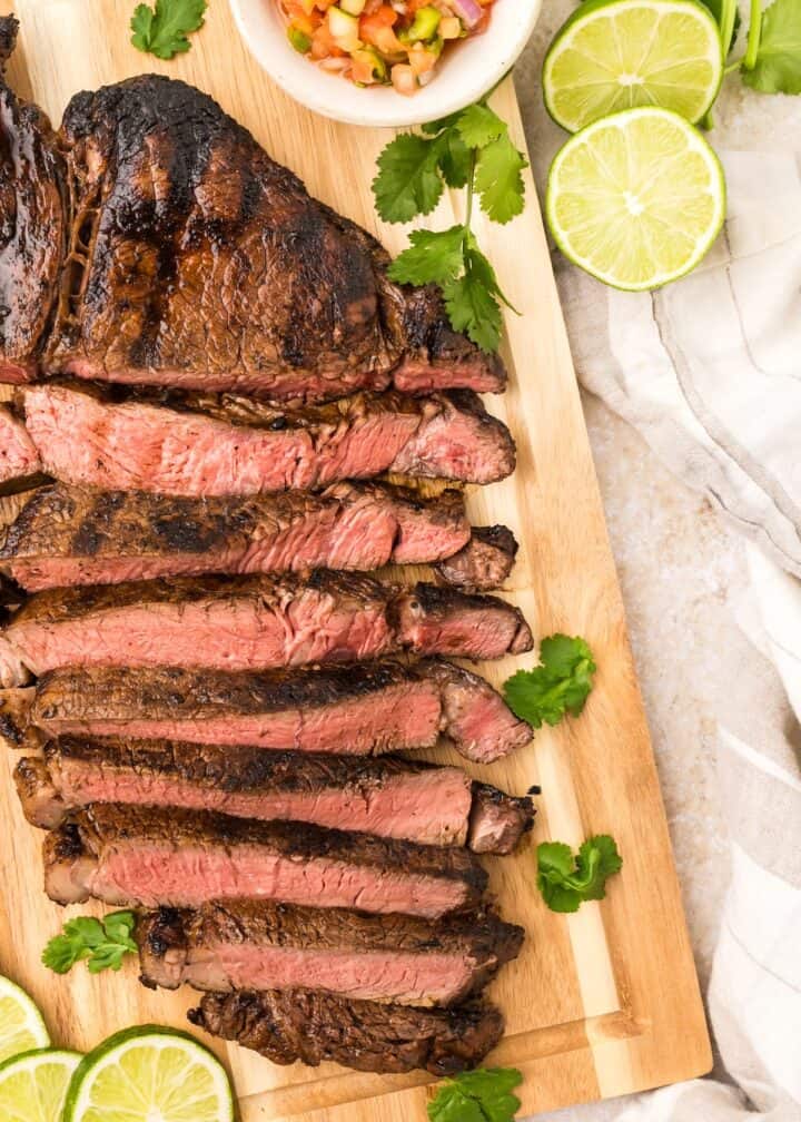 Carne Asada (Mexican Steak) on a cutting board with fresh limes and herbs