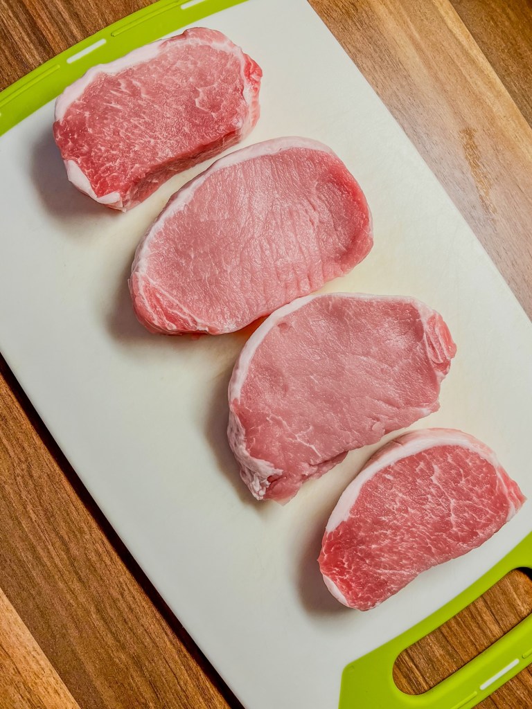 Four pork chops on a cutting board on a wood counter