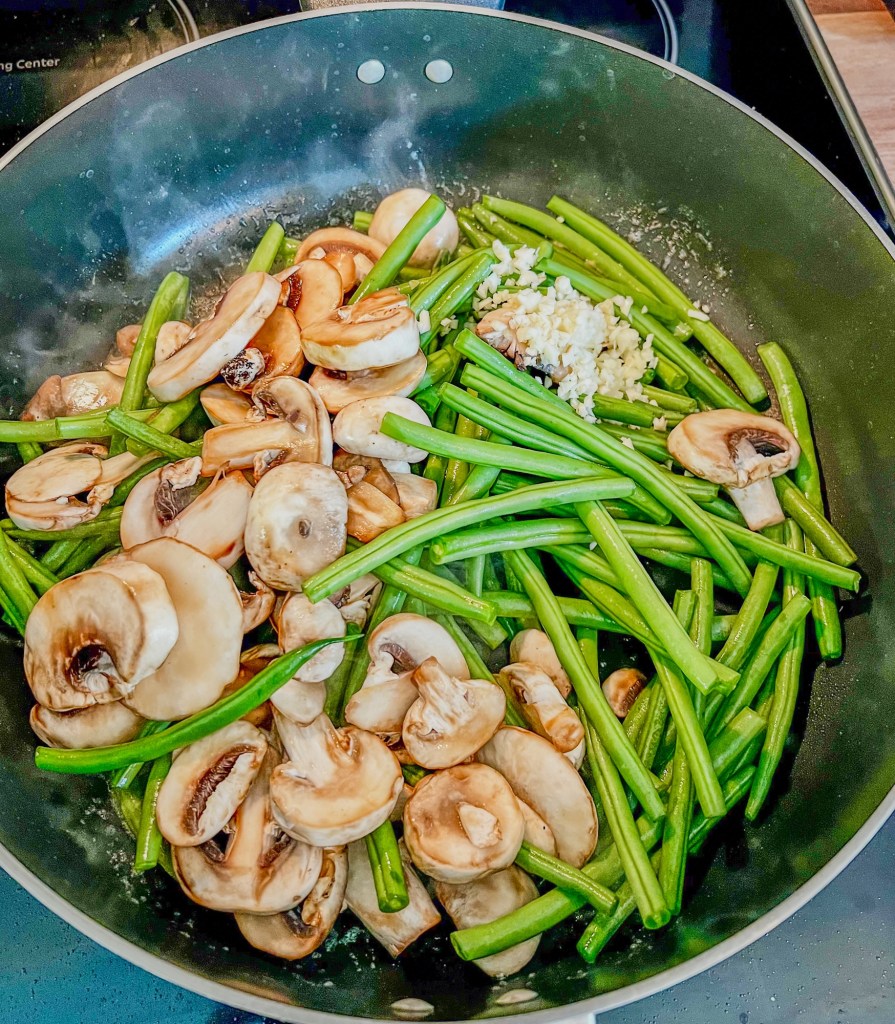 Some mushrooms, green beans, garlic, and butter in a skillet on the stove