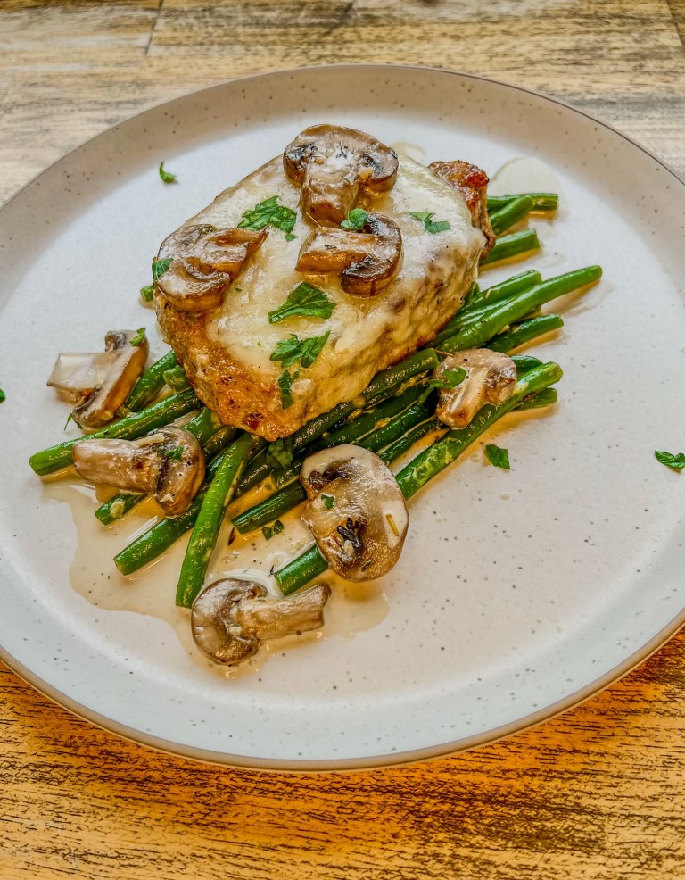Mushroom Swiss Pork Chop with green beans and creamy mushroom sauce on a white plate