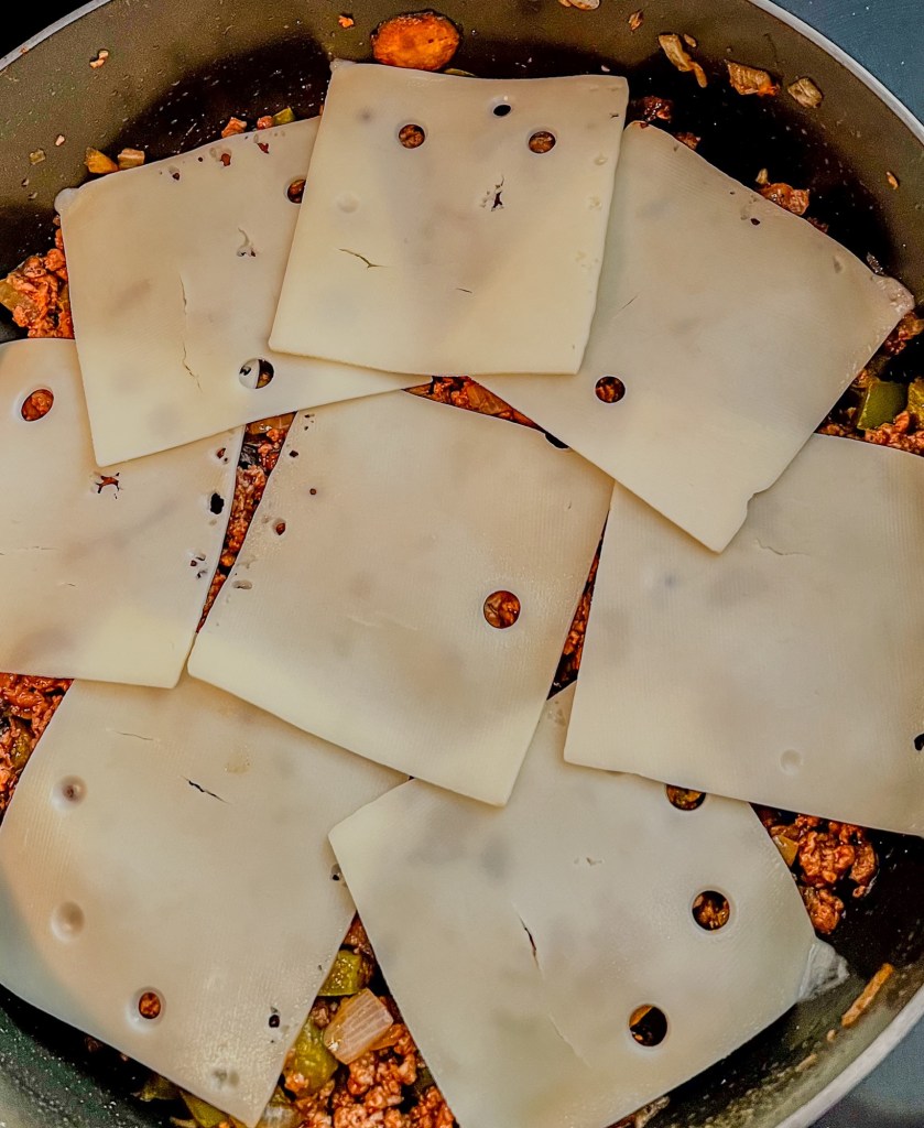 Mushroom sloppy joe mix with swiss cheese layered over the top in a skillet