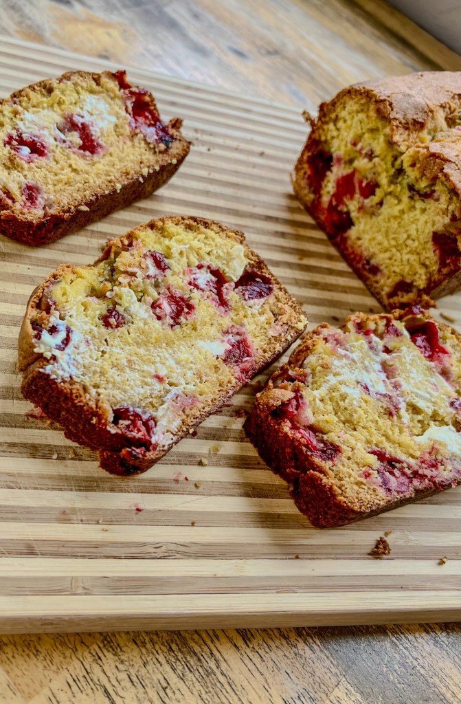 Orange cranberry bread that's been sliced and buttered on a wooden cutting board