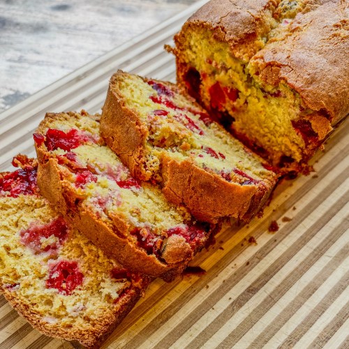 A cranberry orange bread loaf that's been sliced, on a wooden cutting board
