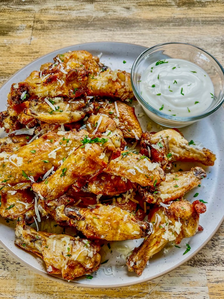 Parmesan Garlic Wings on a white plate with a ramekin of ranch sauce on a wood table
