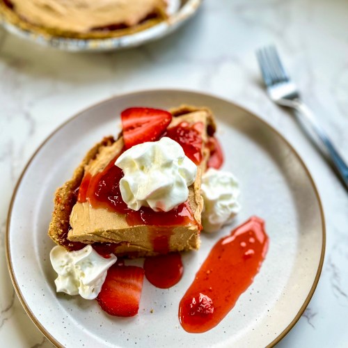 Peanut butter and jelly pie on a plate with some whipped cream and compote on top, with more of the pie behind