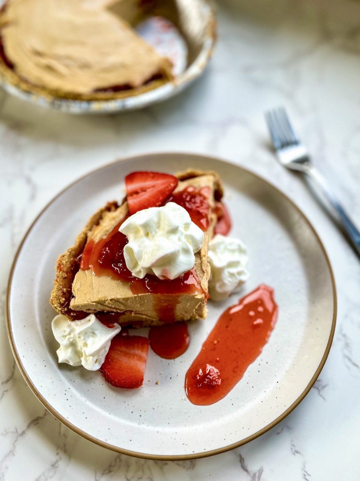 Peanut butter and jelly pie on a plate with some whipped cream and compote on top, with more of the pie behind