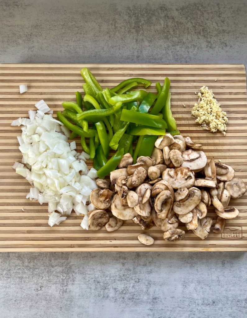 Onion, garlic, mushroom, and green pepper chopped up on a wooden cutting board