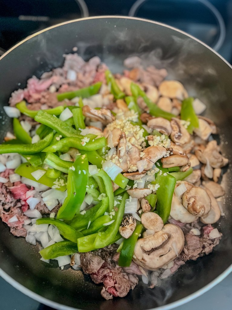 A large skillet filled with steak, pepper, onion, garlic, mushrooms, and seasonings