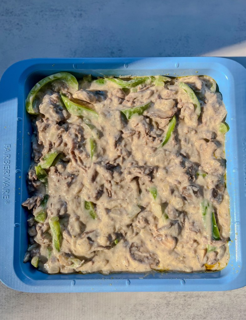 All of the filling ingredients for Philly Cheesesteak Casserole in a baking dish getting ready for the oven