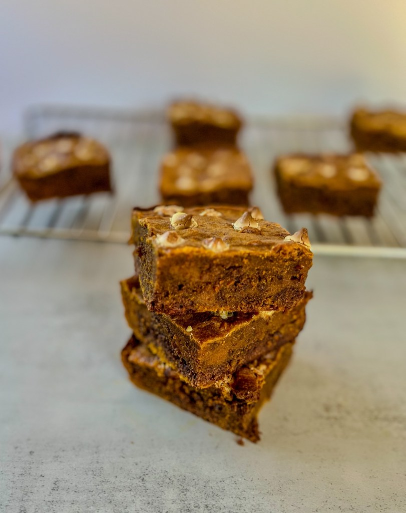 Three brownies stacked up in front of a cooling rack with more brownies on it