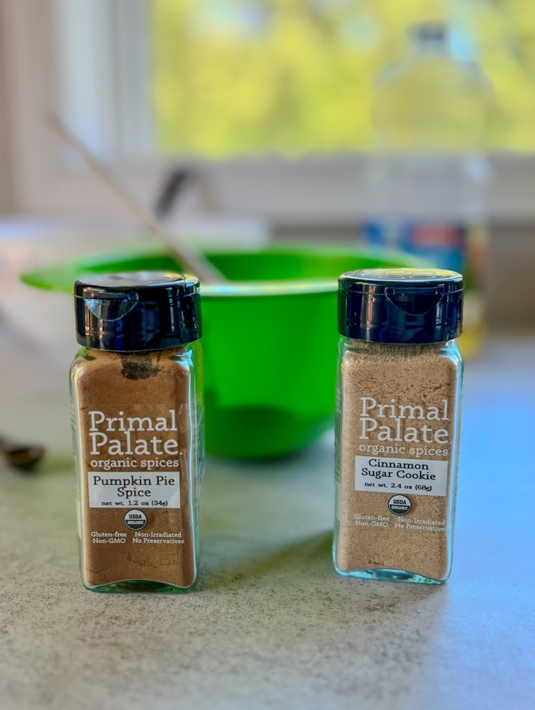 Two bowls filled with pumpkin brownie batter with some primal palate spices in front of them