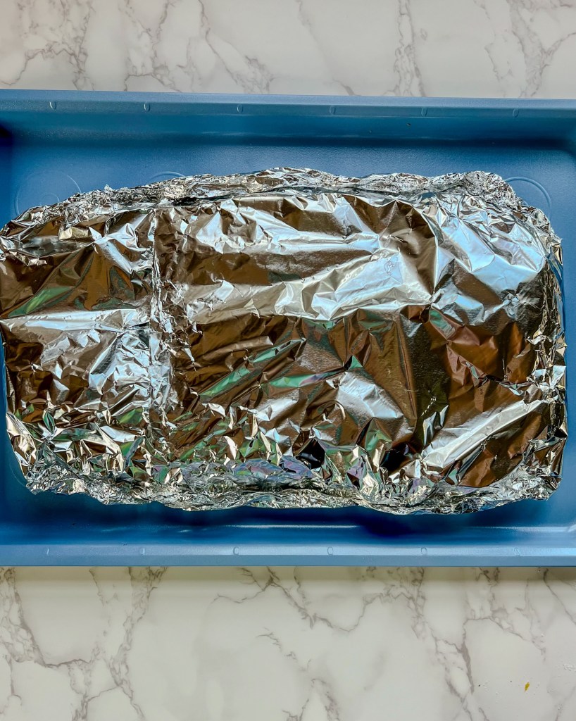 Salmon and broccoli foil pack on a blue baking sheet ready for grilling