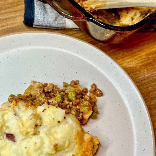 Shepard's pie in a large baking dish with a helping scooped onto a white plate in front of it