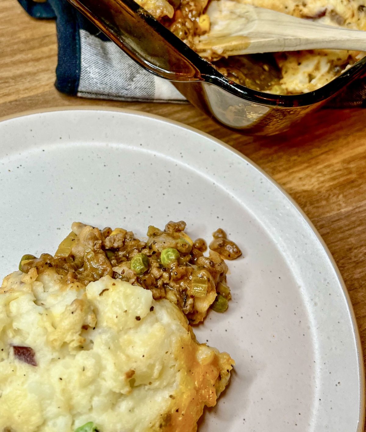 Shepard's pie in a large baking dish with a helping scooped onto a white plate in front of it