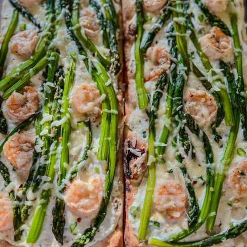 Two flatbreads with shrimp and asparagus on them on a wooden cutting board