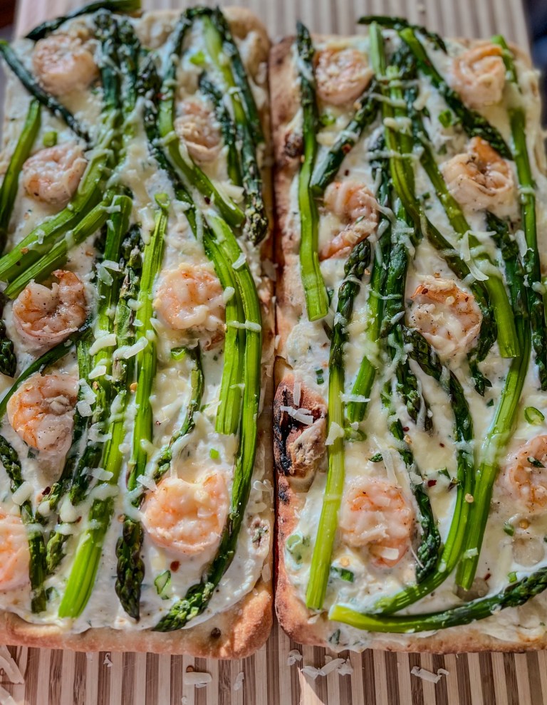 Two flatbreads with shrimp and asparagus on them on a wooden cutting board