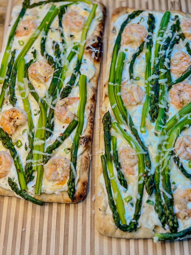 Shrimp and asparagus flatbreads sitting side by side on a wooden cutting board
