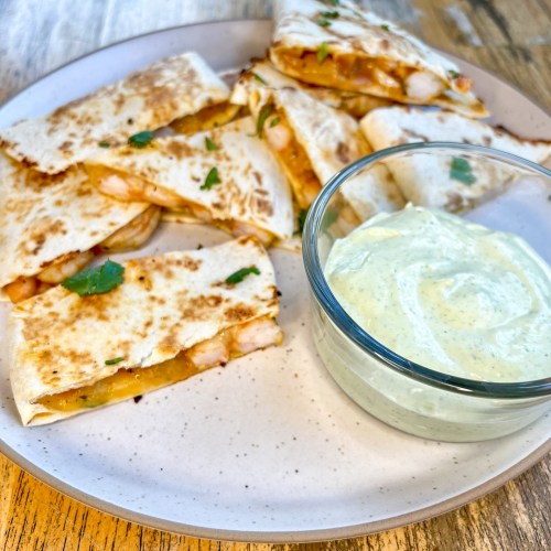 Shrimp quesadillas on a white plate with a side of cilantro lime crema next to it