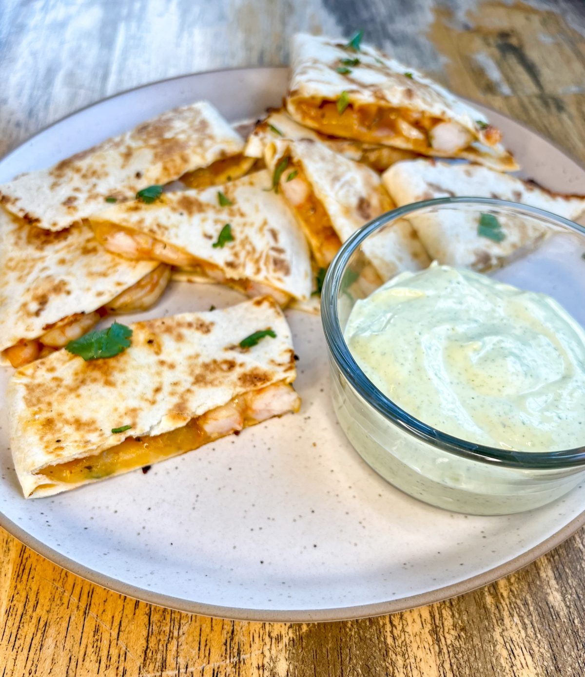 Shrimp quesadillas on a white plate with a side of cilantro lime crema next to it