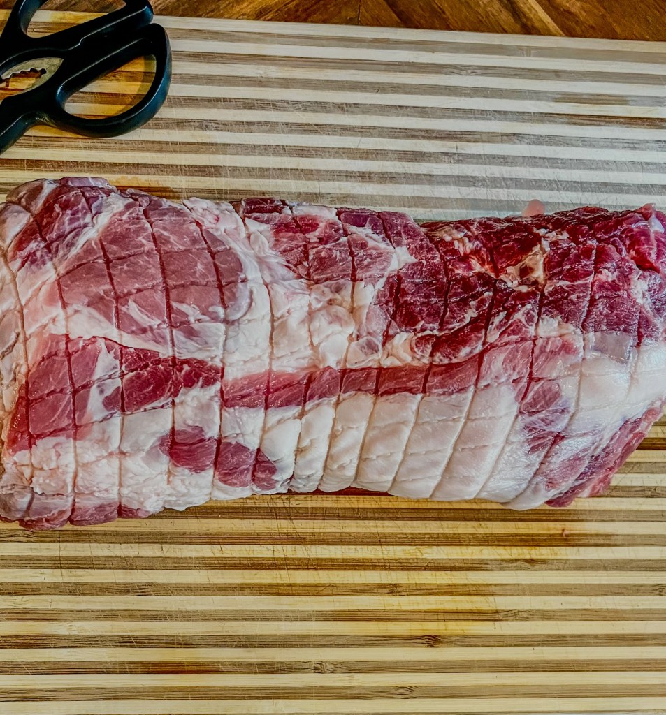 Pork shoulder on a wood cutting board with some scissors nearby