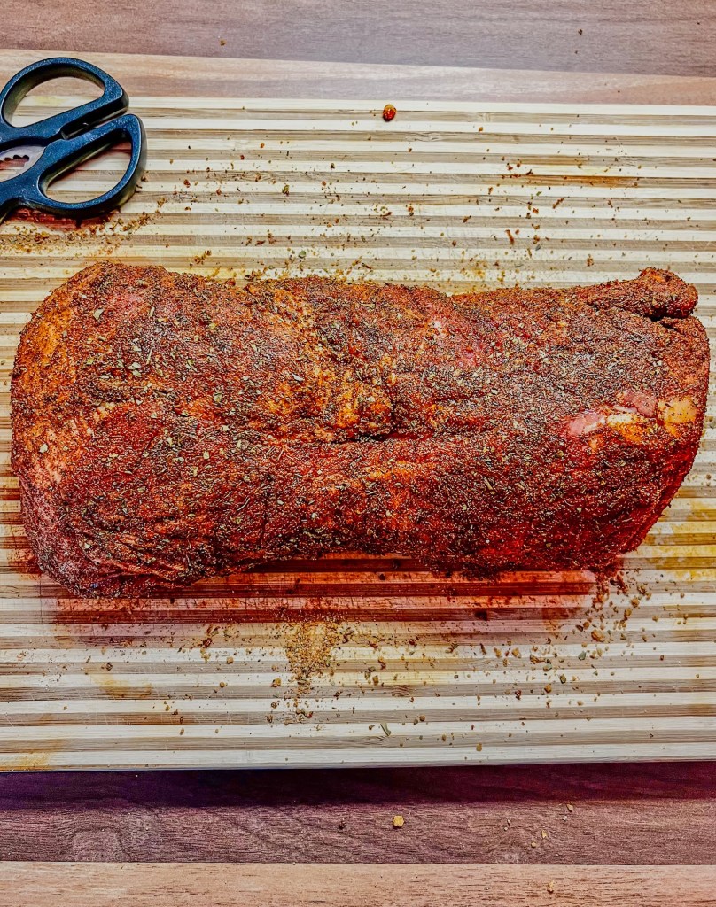 Pork shoulder with a bunch of spices rubbed all over it on a wooden cutting board