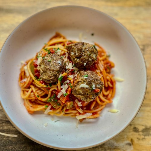 Spaghetti and Meatballs in a white bowl with parsley and parmesan for garnish on a wood table