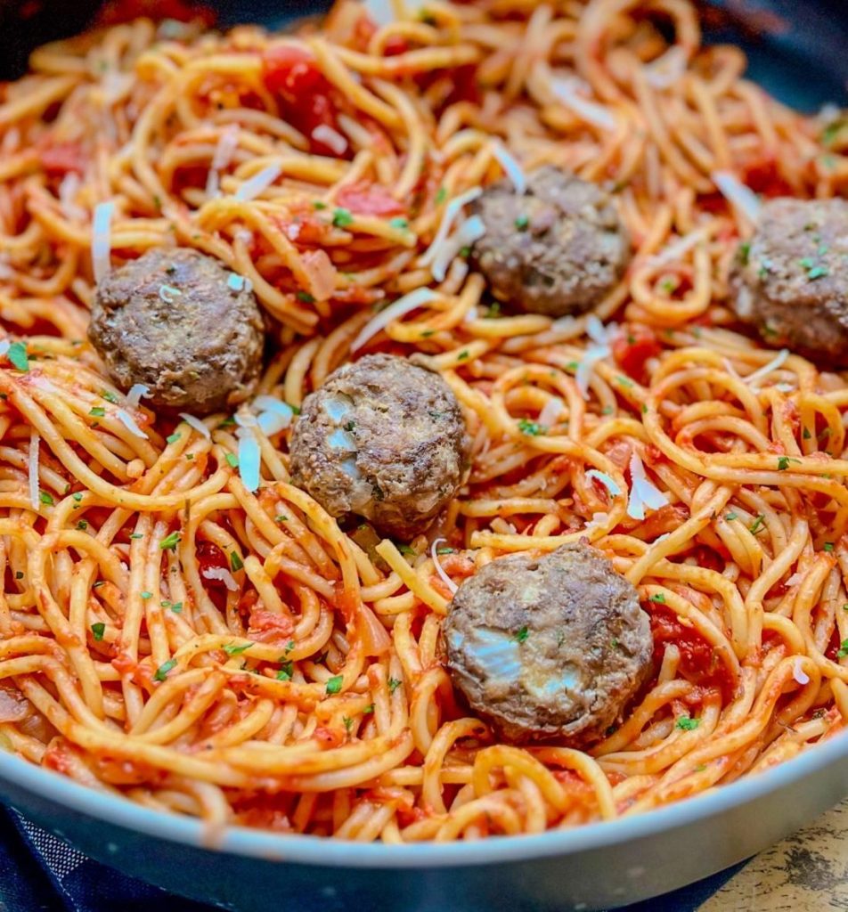Spaghetti and Meatballs in a skillet with a wooden spoon in the pan on a hot pad on a wood table