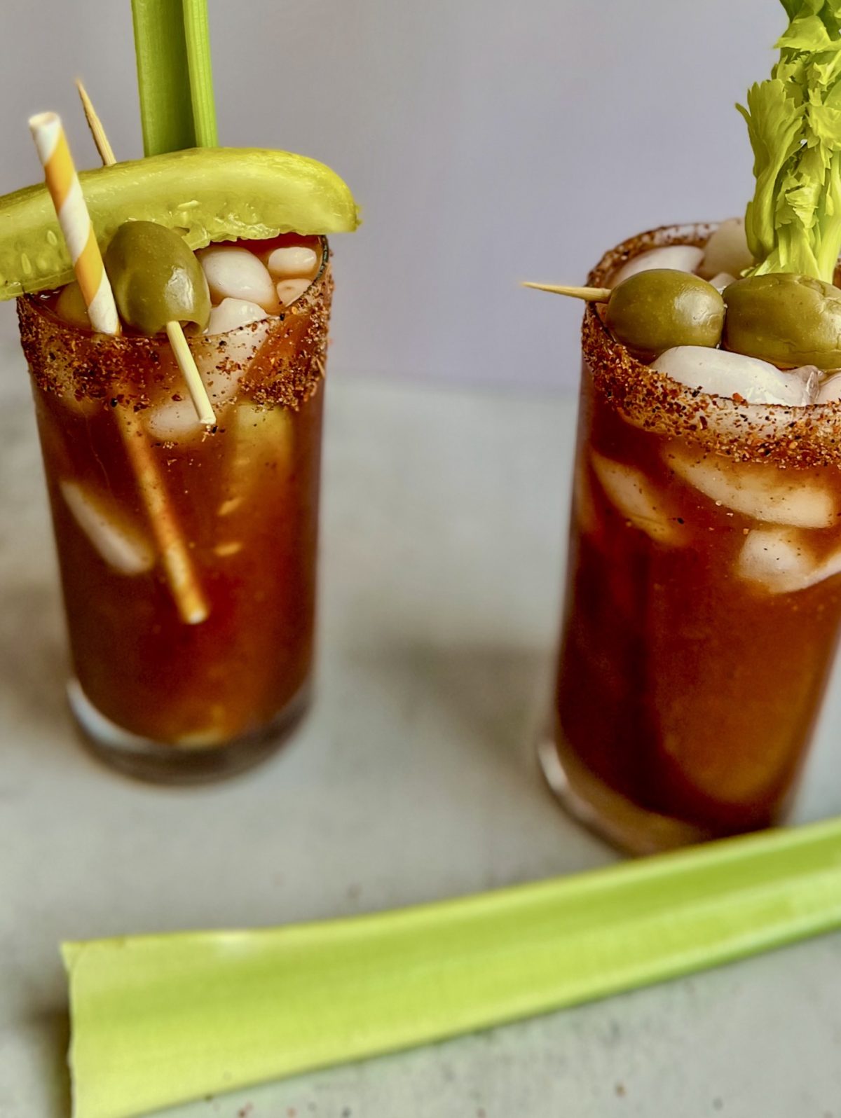 Two Spicy bloody mary drinks with garnishes on a countertop