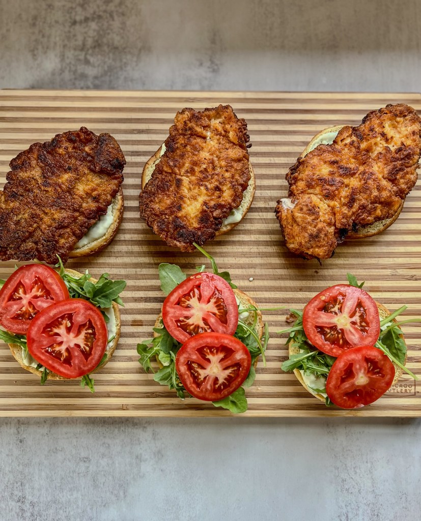 Spicy fried chicken sandwiches being assembled on a wood cutting board