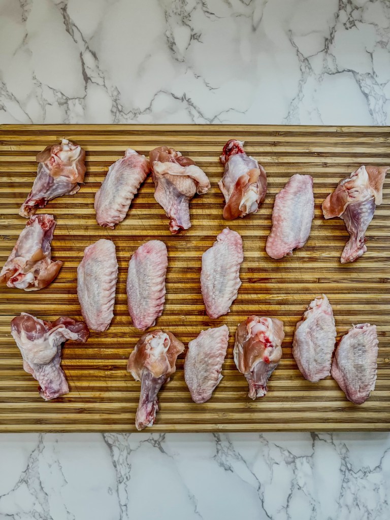 Chicken wings that have been split and pat dry on a wooden cutting board
