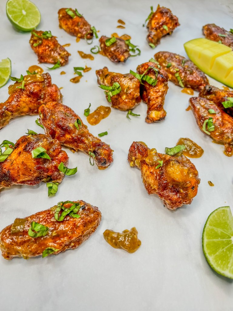 Spicy mango chicken wings with some lime, basil, and mango scattered around them