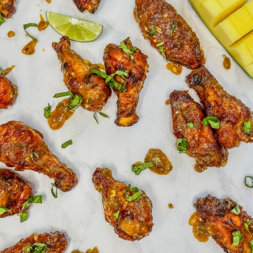 Spicy mango chicken wings with some lime, mango, and basil scattered around