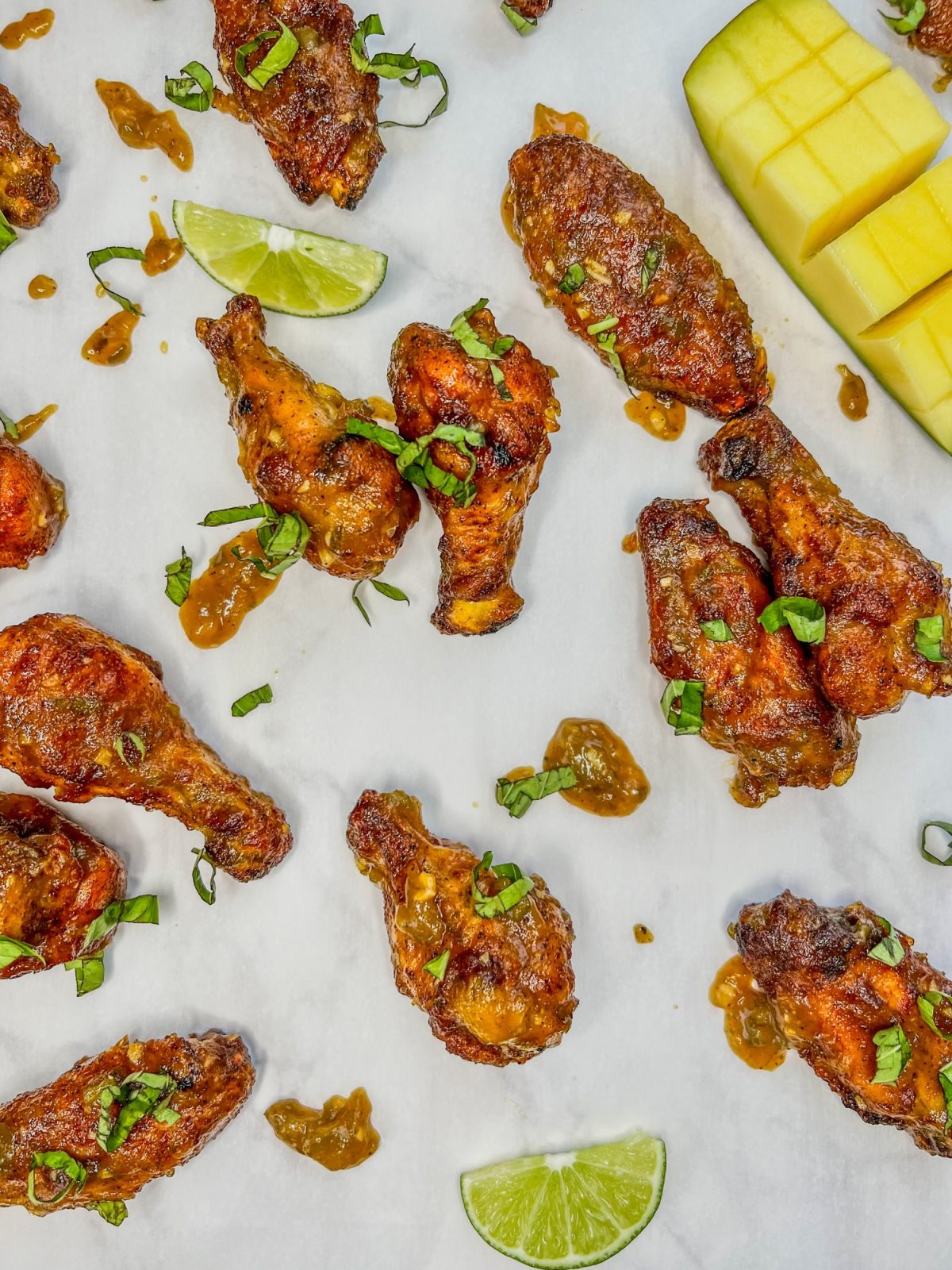 Spicy mango chicken wings with some lime, mango, and basil scattered around