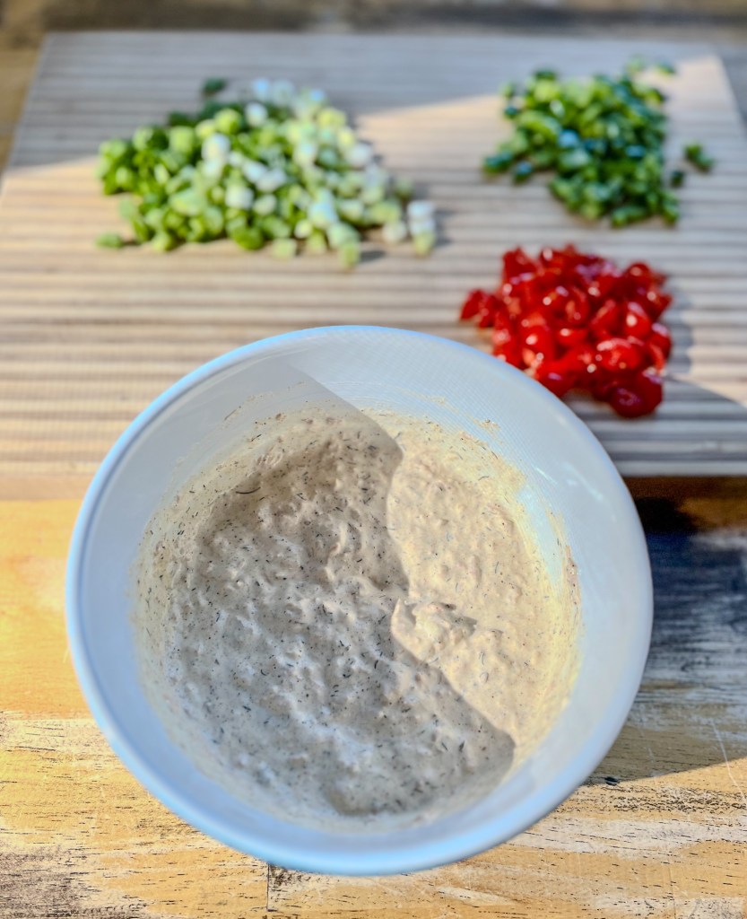 A large bowl filled with the ingredients for tuna pasta salad with some veggies behind on a cutting board