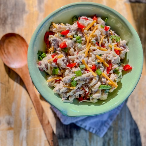 Spicy Tuna Pasta Salad in a large green bowl with a wooden spoon next to it on a wooden table