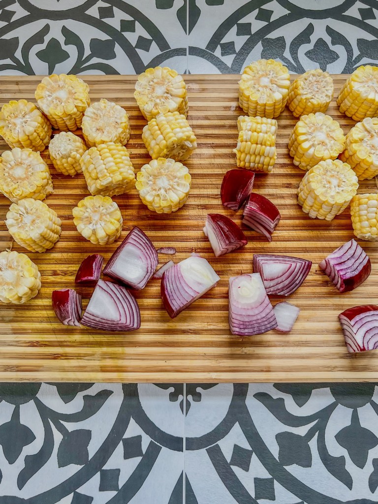 Red onion and fresh ears of corn chopped up on a cutting board