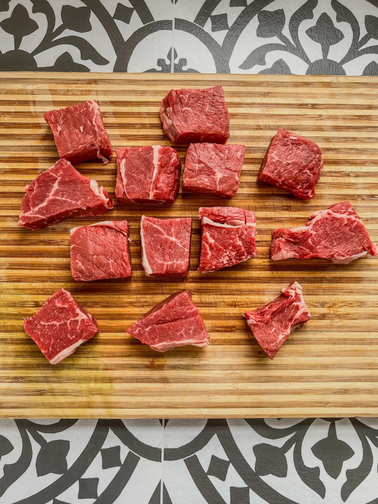 Sirloin steak cut up into large chunks on a cutting board